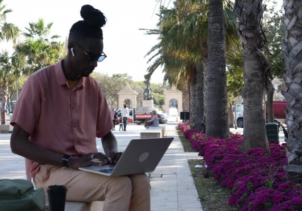 24-160 Black Latino American freelancer sitting on a concrete bench in the park and using a laptop to work remotely